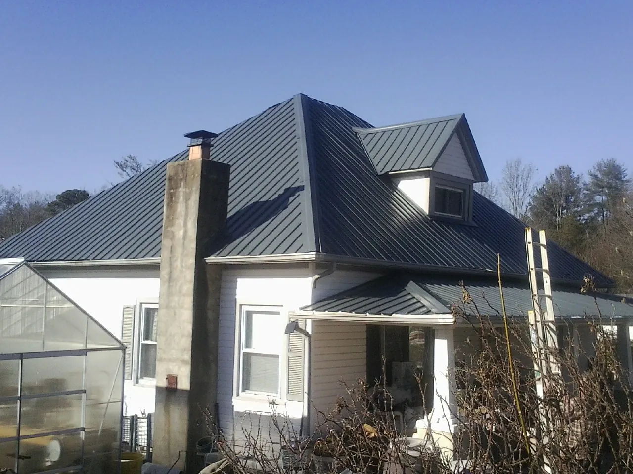 Dark blue standing seam metal roof on a white farmhouse with dormer — Slate & Tile Roof Repair by Roofing Brothers in Mineral City