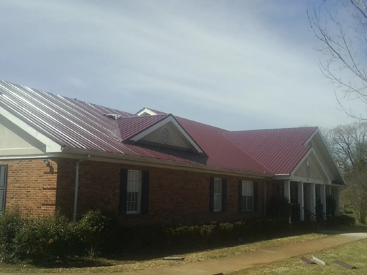 Red metal roof with gabled entries on a long brick building, from a Hail Damage Roof Repair job in Mineral City