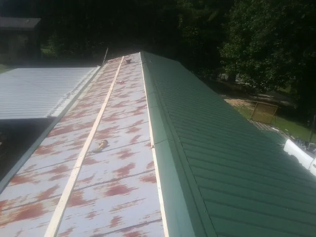 Old rusted panels beside newly installed green metal roofing — Wind Damage Roof Repair by Roofing Brothers in Mineral City