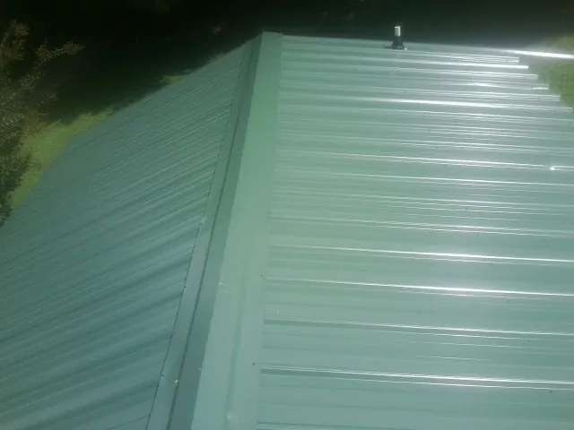 New green metal panels meeting at the ridge of a roof — Flat Roof Repair work by our crew in Mineral City