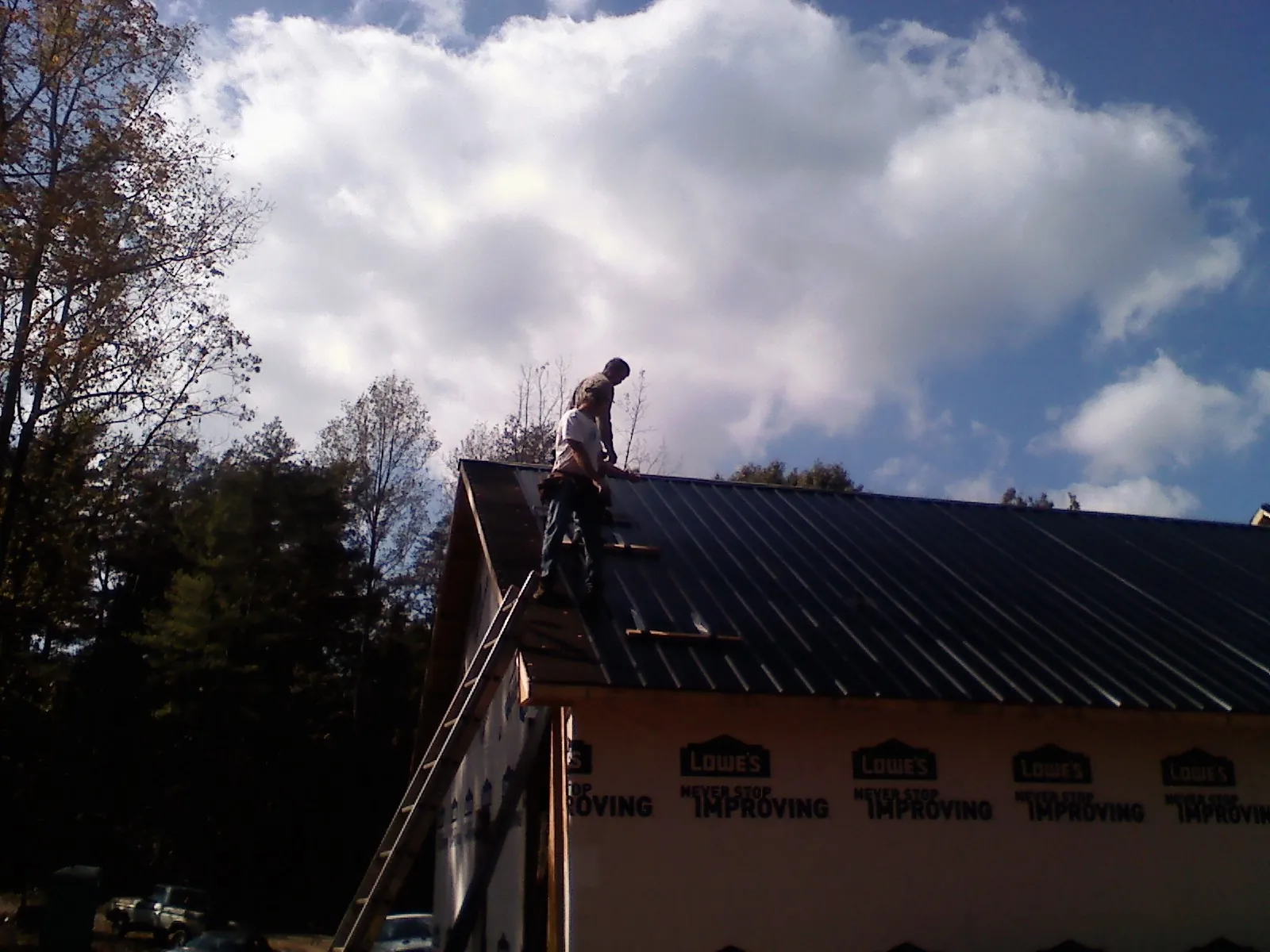 Roofer fastening dark metal panels high against a cloudy sky, from a Roof Inspection job in Mineral City