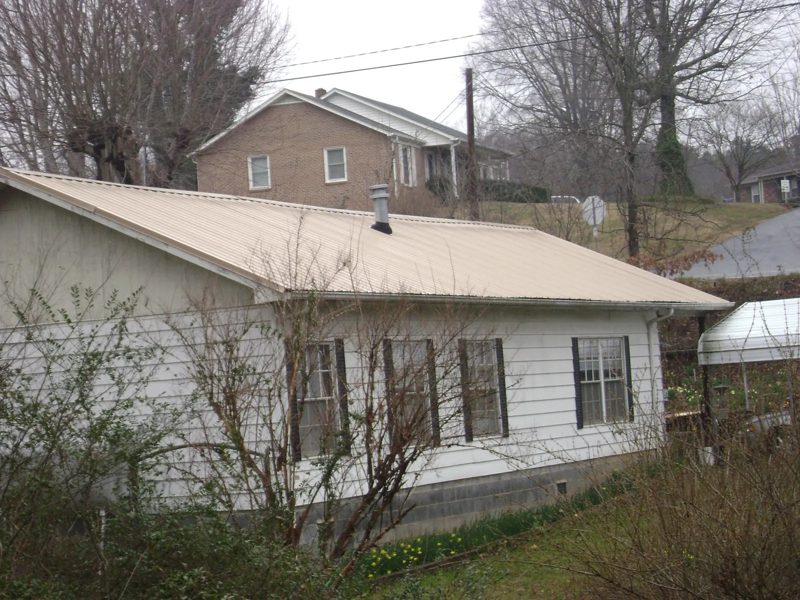 Tan metal roof on a white sided house set into a hillside — Commercial Roofing by Roofing Brothers in Mineral City