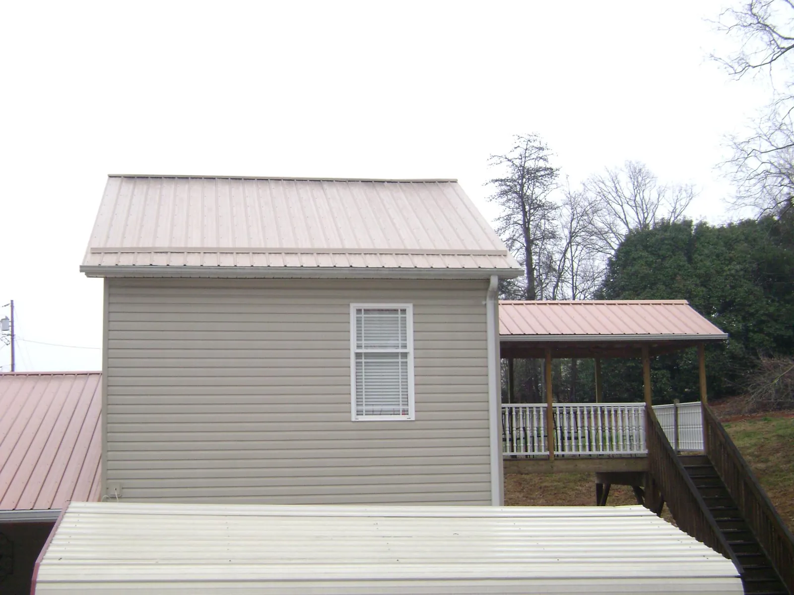 Tan metal roofs on a two story addition and attached porch, from a Roof Replacement job in Mineral City